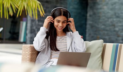 Image of a girl on her headphones looking at her laptop. 